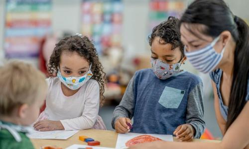 A group of kids at childcare drawing at a table with a staff member