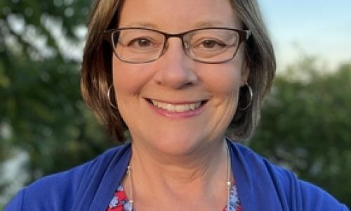 Photo of Megan DeFranco, blue and red shirt, outdoor background, glasses smiling