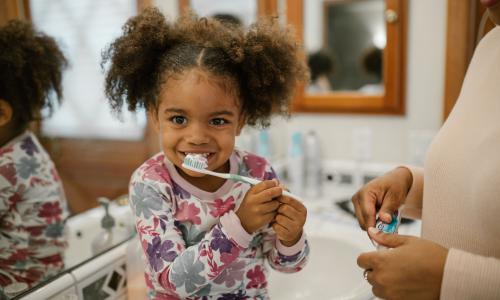 Young girl brushing teeth with mom