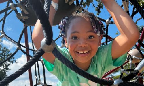 Child wearing a YMCA summer camp shirt plays on a playground