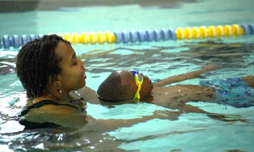 YMCA swim instructor assisting child with swimming lesson