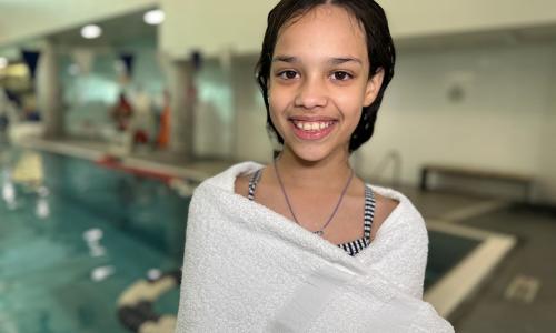 Child standing wrapped in a towel in the YMCA pool area