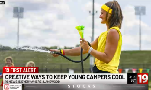 Camp counselor spraying camper with garden hose