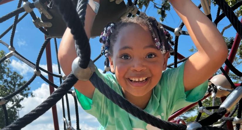 Child wearing a YMCA summer camp shirt plays on a playground