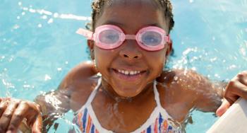 Little girl swimming in pool with goggles, smiling.
