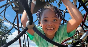 Child wearing a YMCA summer camp shirt plays on a playground