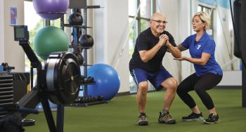 YMCA staff member assisting an older adult with fitness training in a YMCA facility.